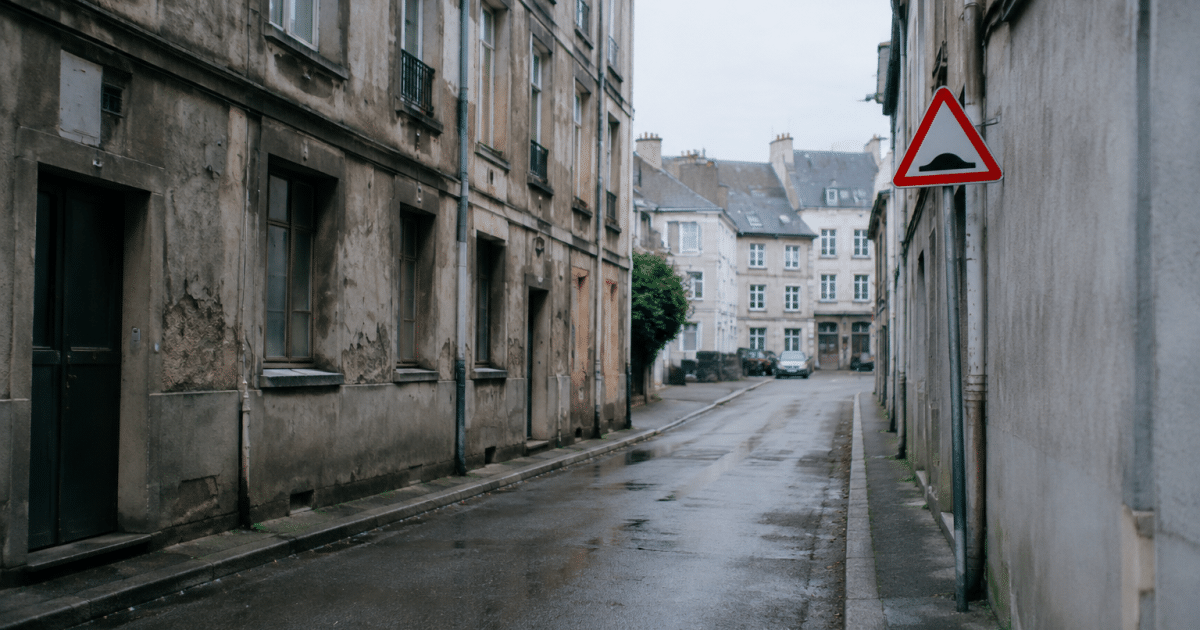 Rue urbaine delimitee par batiments gris delabre avec panneaux danger