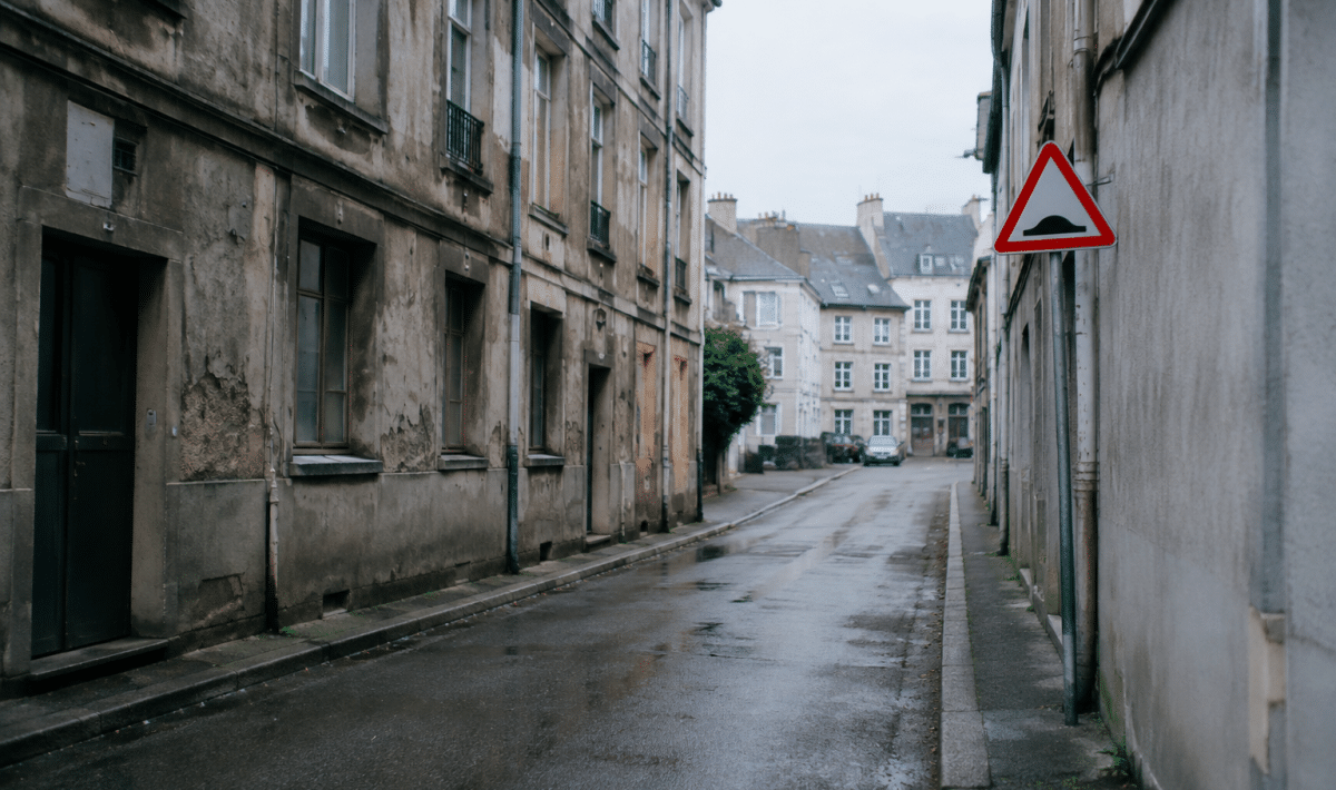 Rue urbaine delimitee par batiments gris delabre avec panneaux danger