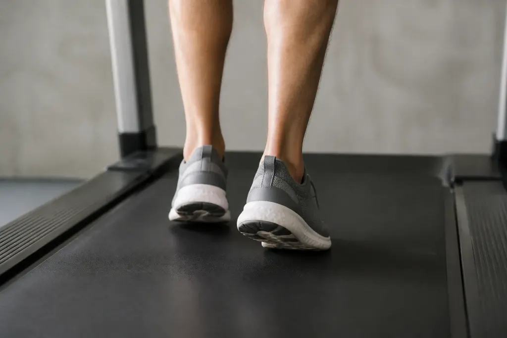 Coureur sur tapis roulant, pieds visibles, chaussures sur fond gris