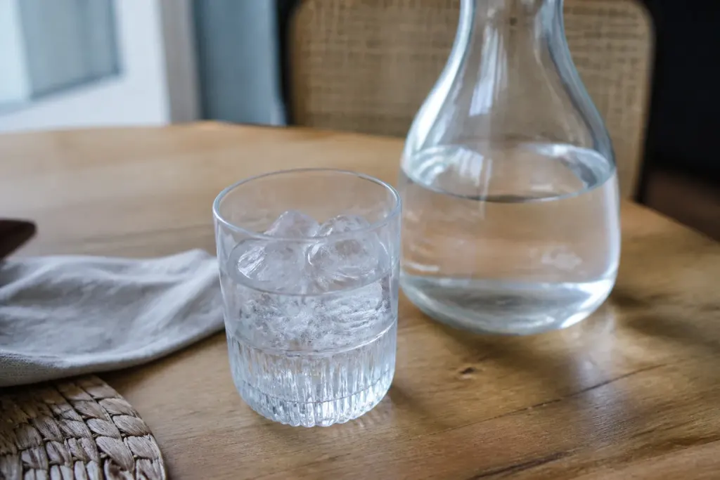 Verre plein de glacons et carafe transparente sur table